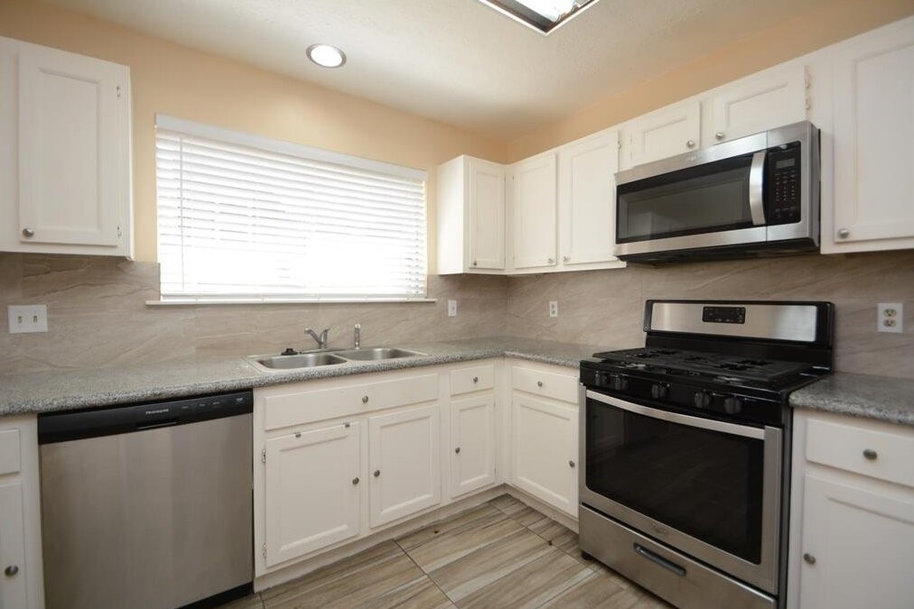 15 South Tallowberry Drive Spring, TX 77381 - Photo 10 of 26 Modern kitchen with stainless steel appliances, white cabinetry, granite countertops, and a large window providing natural light.