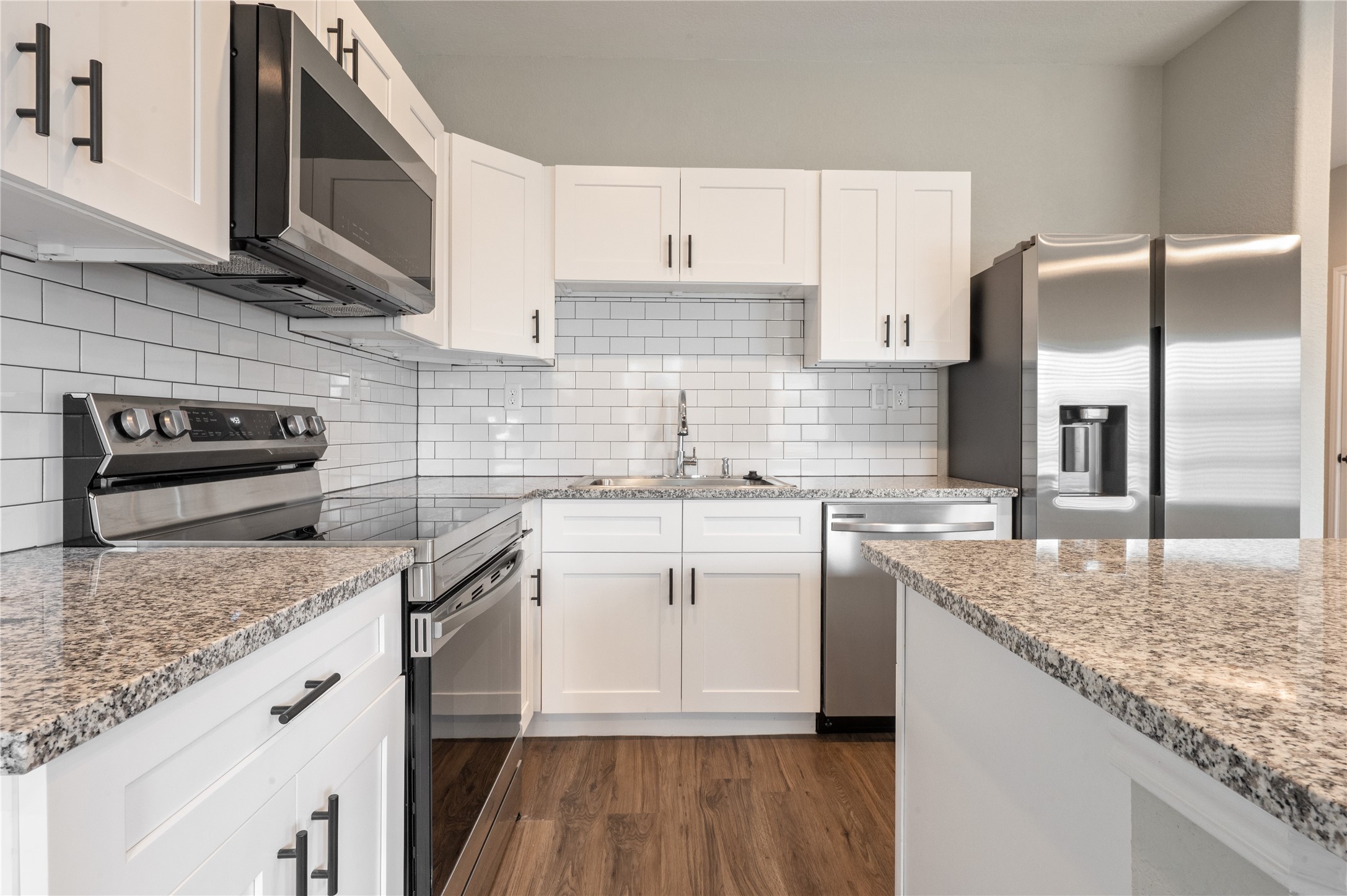 14010 Longstreet Road, Unit 2 Willis, TX 77318 - Photo 20 of 29 Modern kitchen featuring sleek stainless steel appliances, granite countertops, white shaker cabinets, and a stylish subway tile backsplash. Warm wood flooring adds a cozy touch.