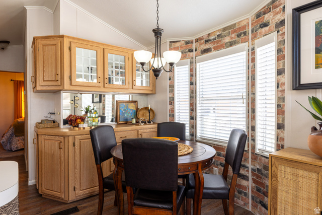 2990 East Riverside Drive, Unit 117 St. George, UT 84790 - Photo 1 of 1 Dining room with vaulted ceiling, ornamental molding, a chandelier, dark wood-style floors, and brick wall