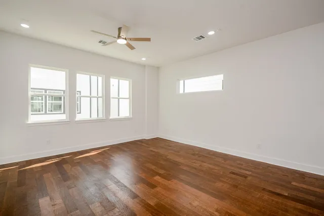 an empty room with wooden floor fan and windows