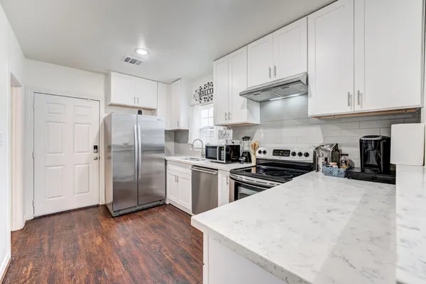 a kitchen with granite countertop a refrigerator oven a sink dishwasher and white cabinets with wooden floor