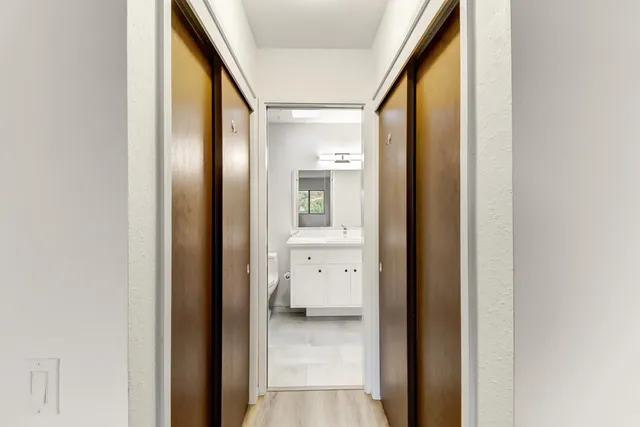 a view of a hallway with wooden floor and a bathroom