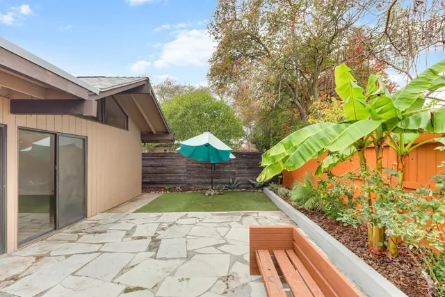 a backyard of a house with table and chairs under an umbrella