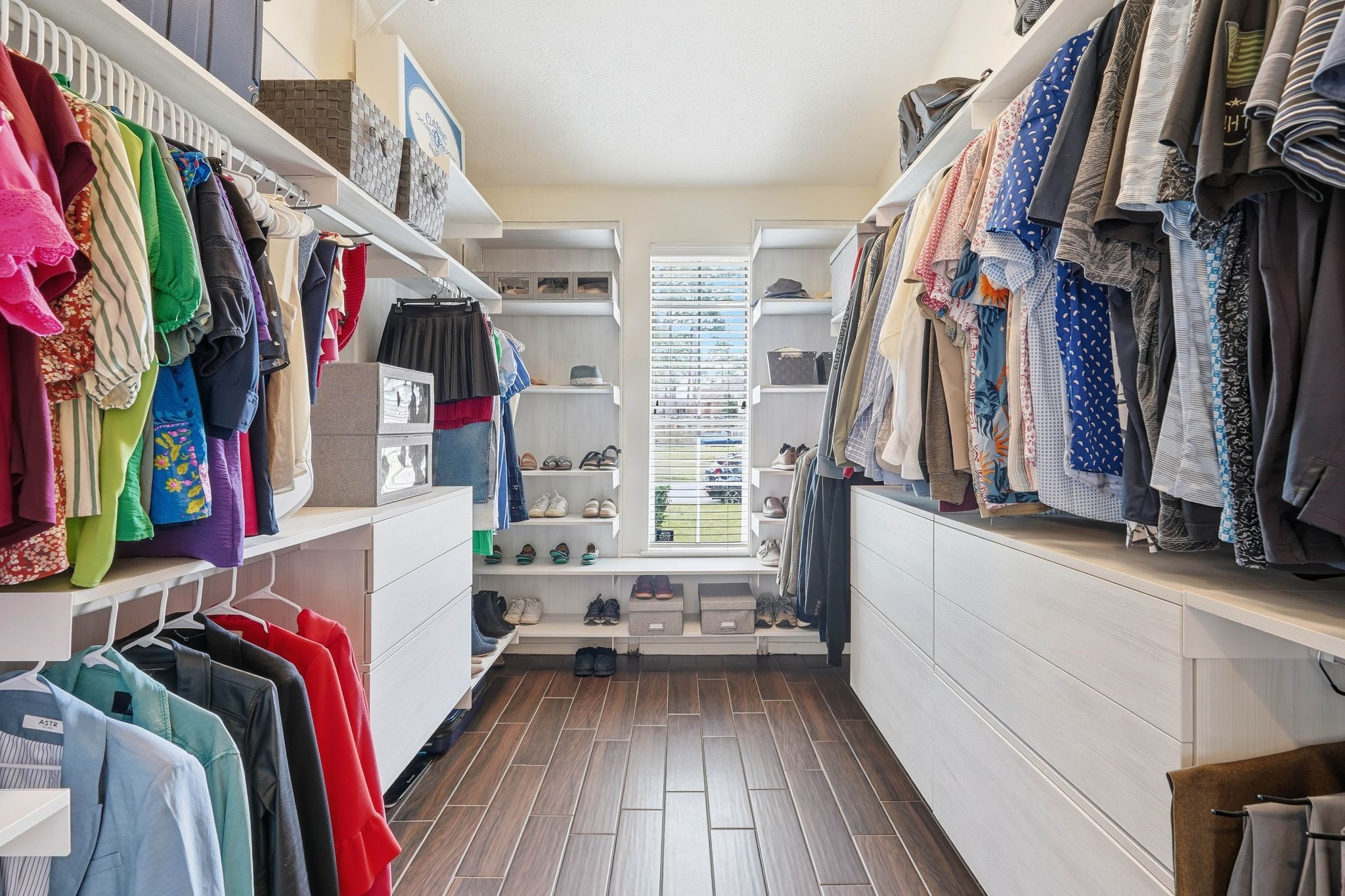 2515 Woodsboro Drive Spring, TX 77388 - Photo 26 of 44 This a spacious walk-in closet in the primary bedroom has ample storage, featuring open shelving, hanging rods, and drawers on both sides. The natural light from a window at the end of the room enhances the bright and organized space.