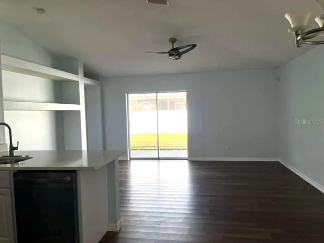 an empty room with wooden floor chandelier fan and windows