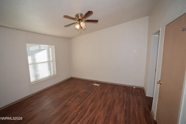 an empty room with wooden floor fan and windows