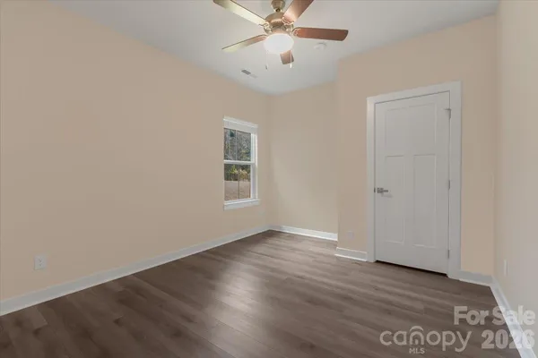 an empty room with wooden floor chandelier fan and windows