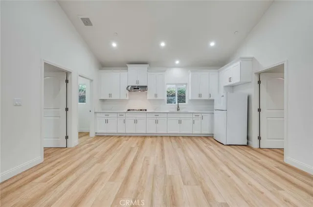 a large kitchen with a refrigerator a sink and wooden floor