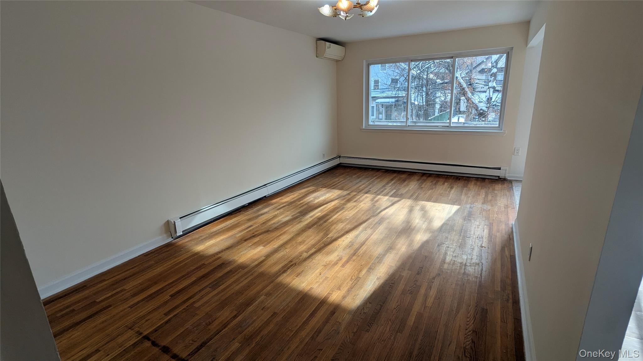 99-47 62nd Road Queens, NY 11374 - Photo 2 of 21 Empty room with baseboard heating, light wood finished floors, and a wall unit AC