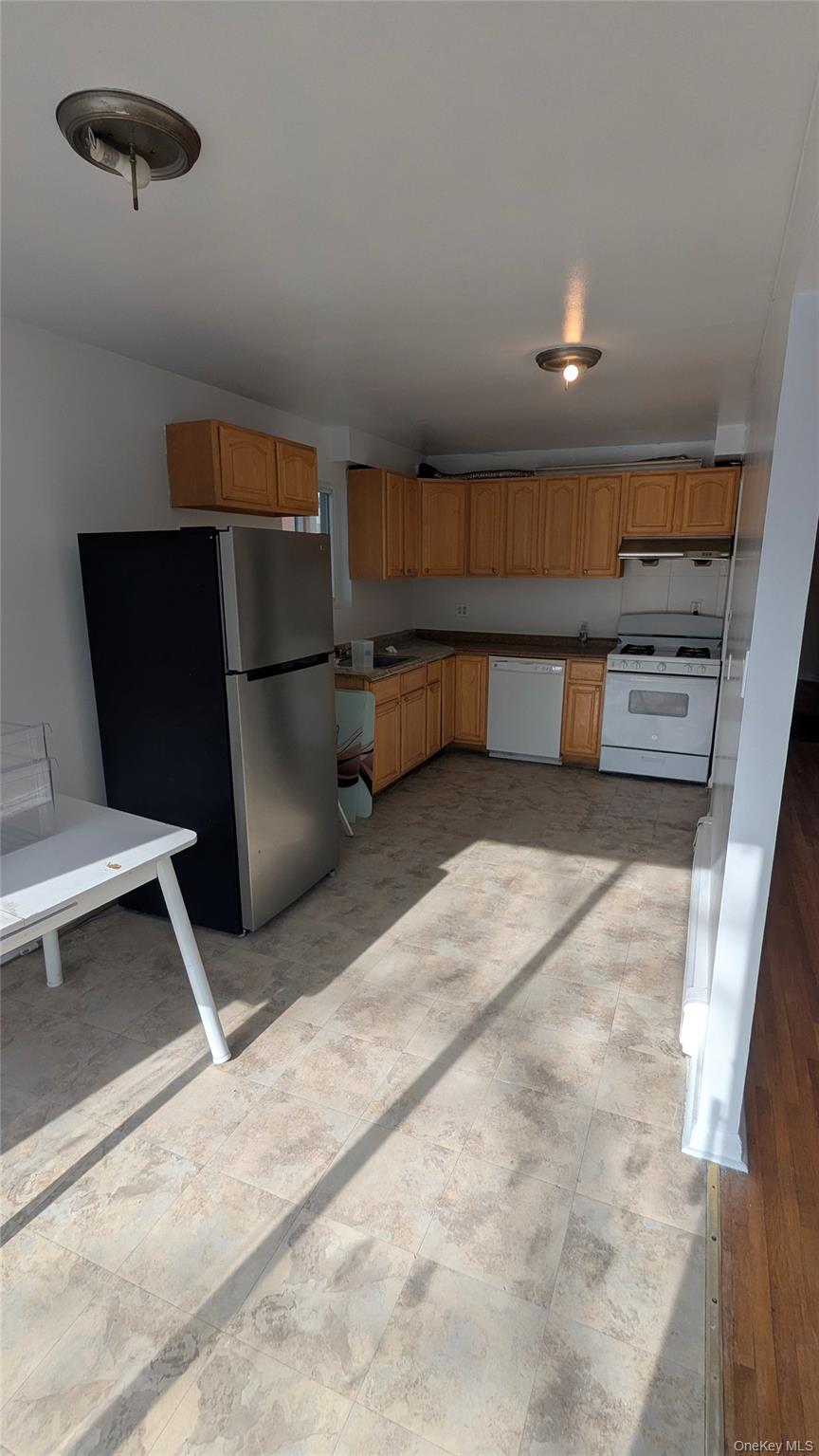 99-47 62nd Road Queens, NY 11374 - Photo 9 of 21 Kitchen featuring white appliances, under cabinet range hood, brown cabinetry, dark countertops, and light floors
