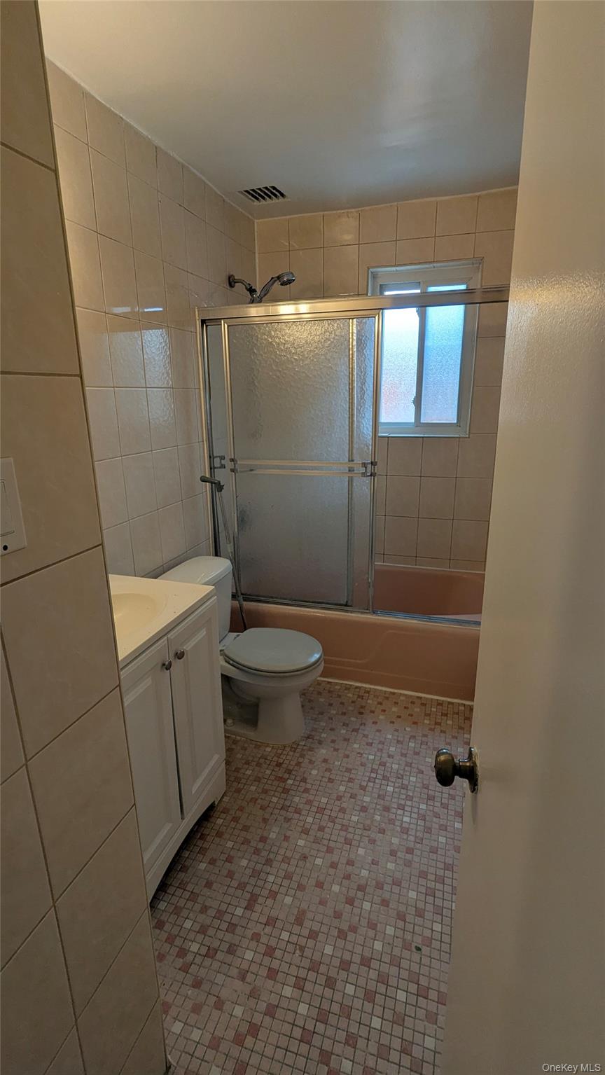 99-47 62nd Road Queens, NY 11374 - Photo 10 of 21 Bathroom featuring vanity, tile walls, shower / bath combination with glass door, and light tile patterned floors