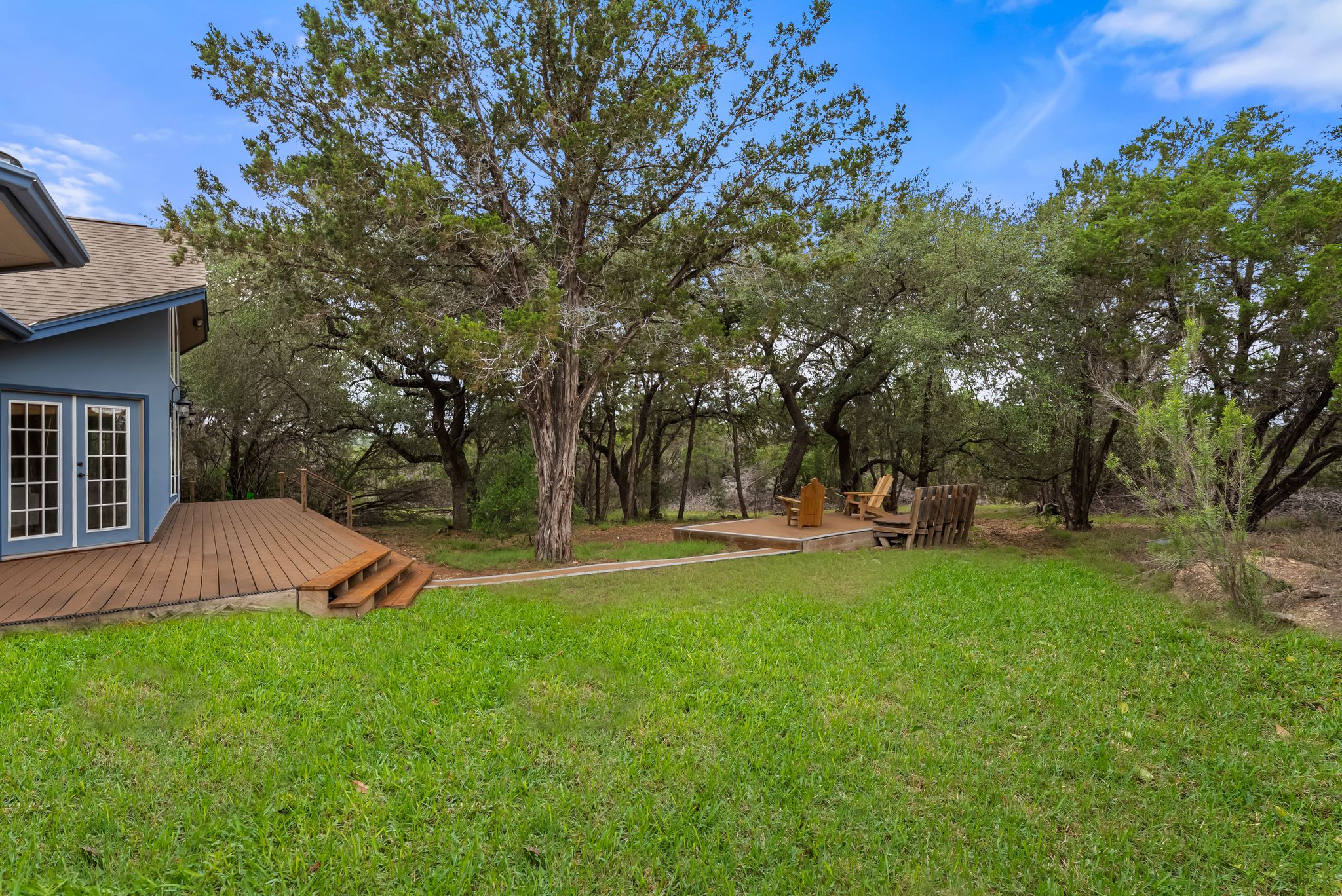 200 Vista West Ranch Road Dripping Springs, TX 78620 - Photo 18 of 20 Expansive outdoor living area featuring a wood-finish deck with integrated steps, double French doors, and mature trees providing natural shade