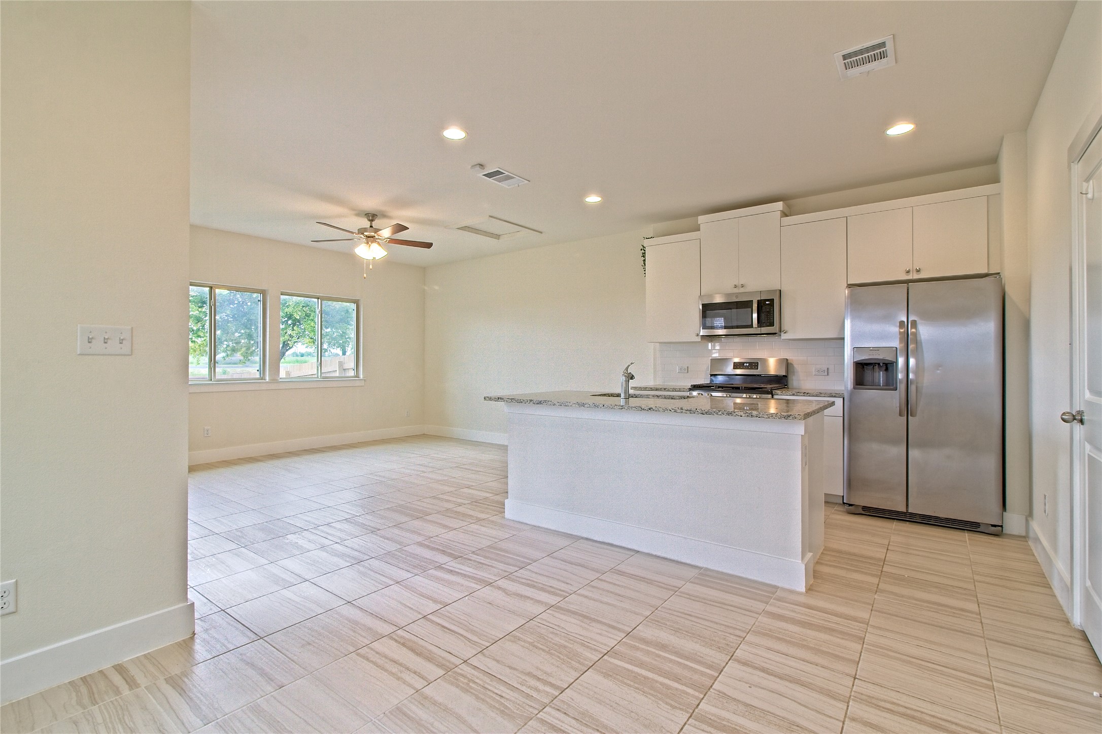 555 White Steppe Way Georgetown, TX 78626 - Photo 7 of 40 Kitchen with stainless steel appliances, white cabinetry, light stone counters, a ceiling fan, and an island with sink