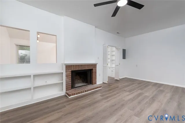 a view of an empty room with wooden floor fireplace and a window