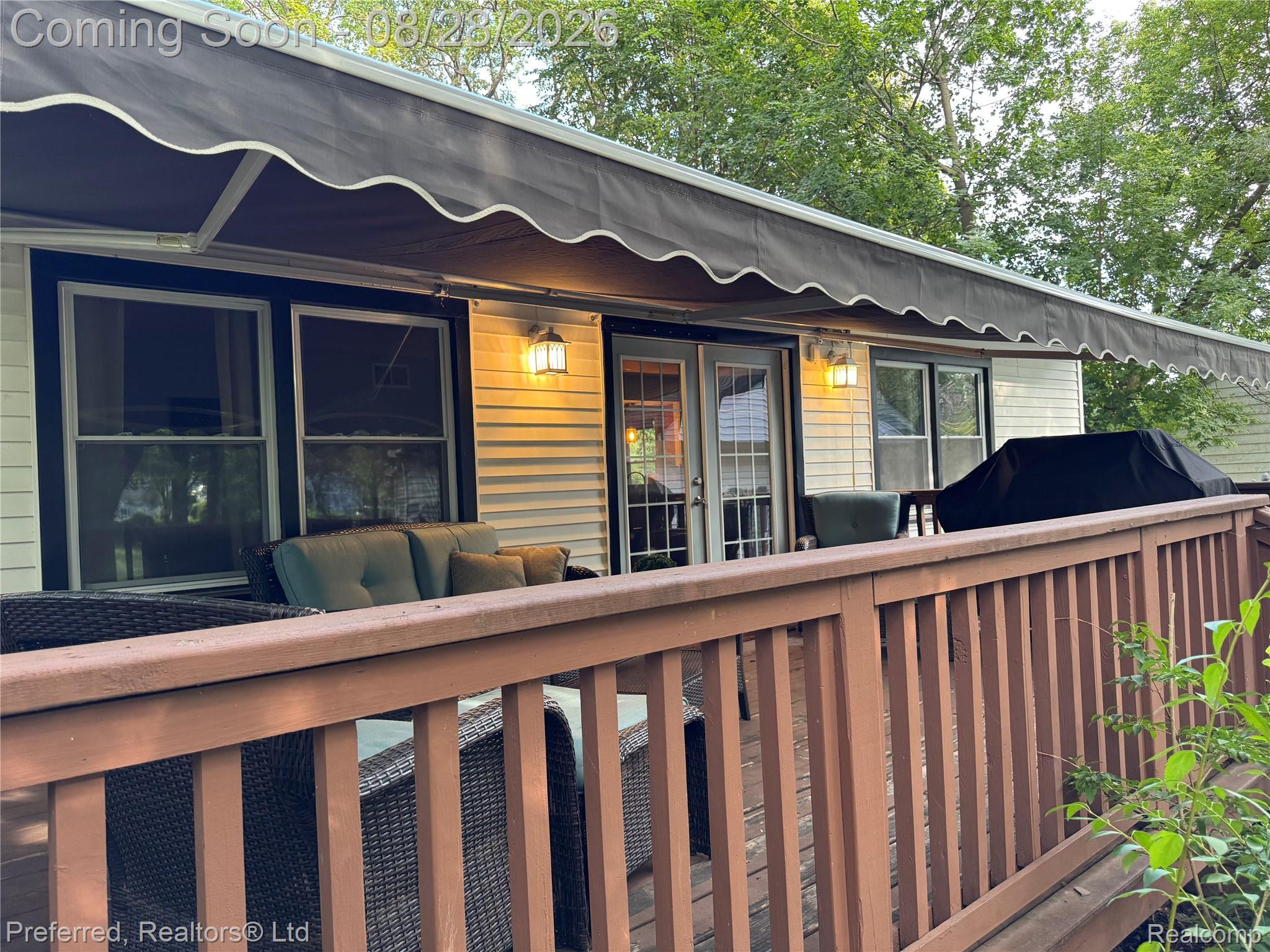 10362 Quirk Road Belleville, MI 48111 - Photo 38 of 41 Exterior wood deck with a brown finish, featuring a full-width retractable awning and exterior wall sconces