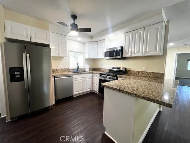 a kitchen with granite countertop a refrigerator a sink dishwasher a stove top oven a refrigerator and cabinets with wooden floor