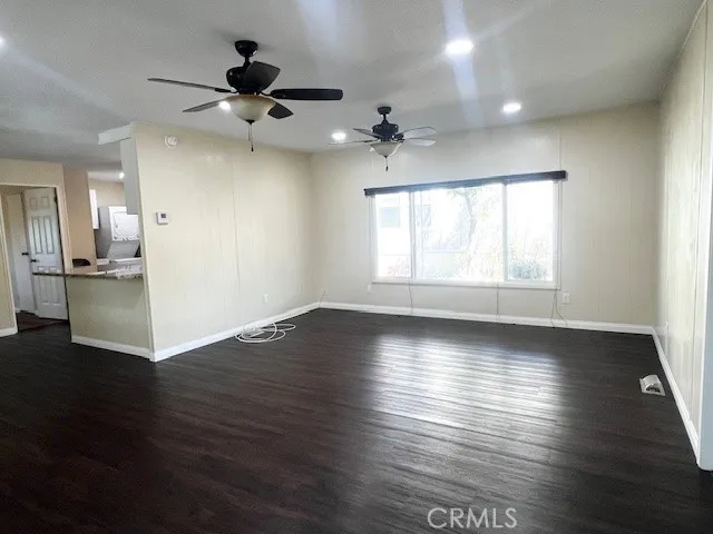 an empty room with wooden floor chandelier fan and windows