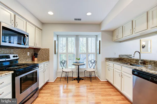 a kitchen with stainless steel appliances granite countertop a stove top oven a sink dishwasher and white cabinets with wooden floor