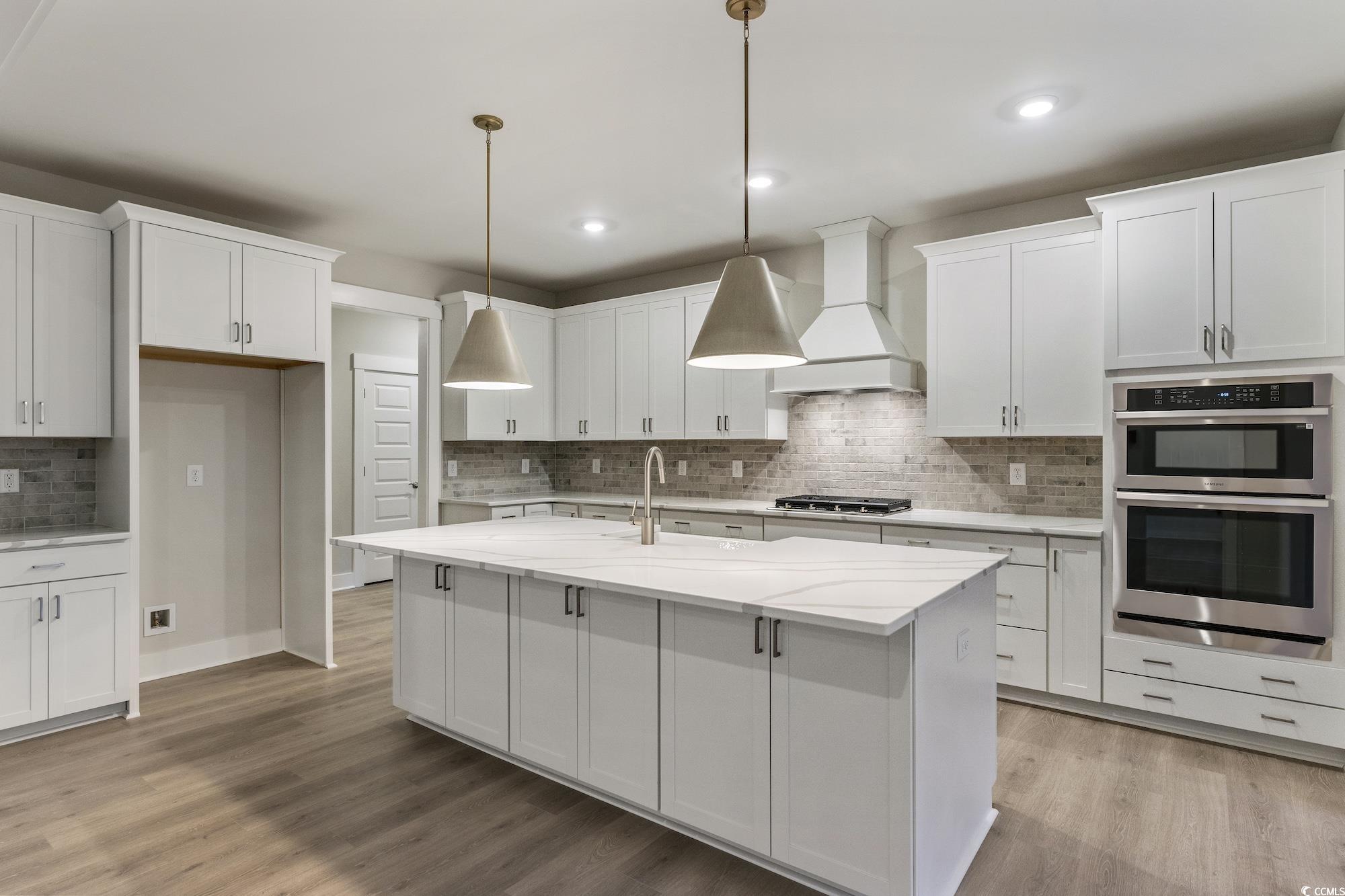 719 Daisy Bank Circle Georgetown, SC 29440 - Photo 11 of 33 Kitchen featuring appliances with stainless steel finishes, white cabinets, custom exhaust hood, backsplash, and light stone countertops