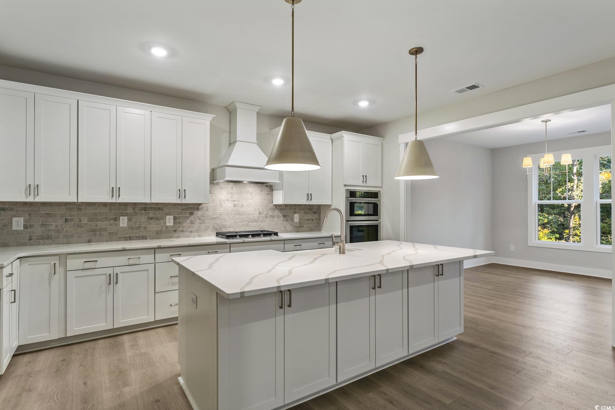 719 Daisy Bank Circle Georgetown, SC 29440 - Photo 12 of 33 Kitchen with white cabinetry, custom exhaust hood, light stone counters, a kitchen island with sink, and light wood-type flooring