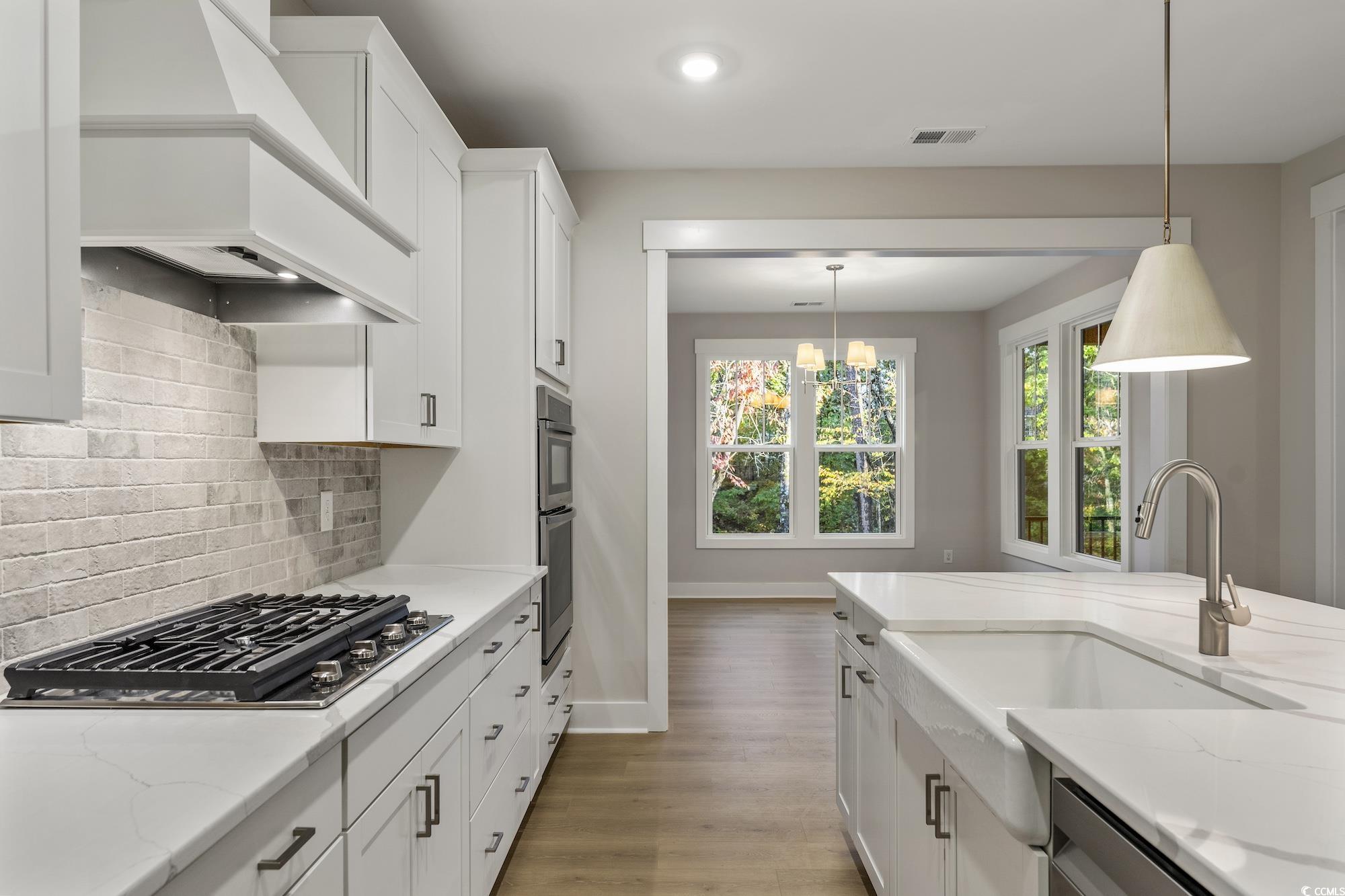 719 Daisy Bank Circle Georgetown, SC 29440 - Photo 13 of 33 Kitchen with white cabinetry, light stone counters, custom range hood, decorative light fixtures, and light wood-style floors