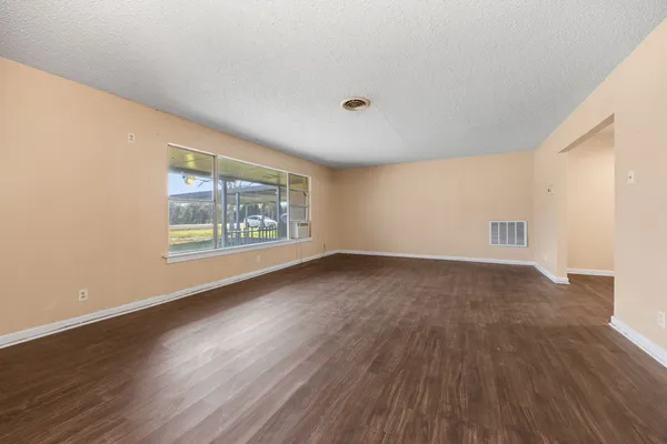 an empty room with wooden floor chandelier and windows