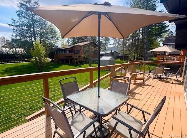 67 West Shore Road Kauneonga Lake, NY 12749 - Photo 16 of 17 Wooden terrace featuring outdoor dining space, a storage shed, an outdoor structure, and a lawn