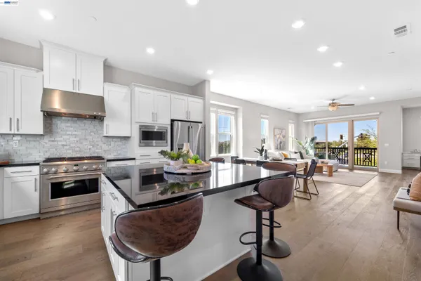 a kitchen with stainless steel appliances granite countertop a stove a sink a refrigerator a stove a dining table and chairs with wooden floor