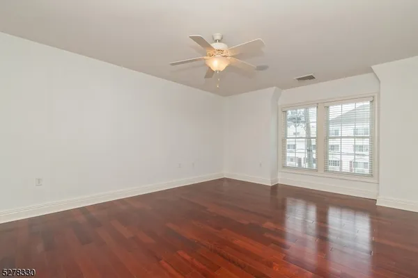 an empty room with wooden floor fan and windows