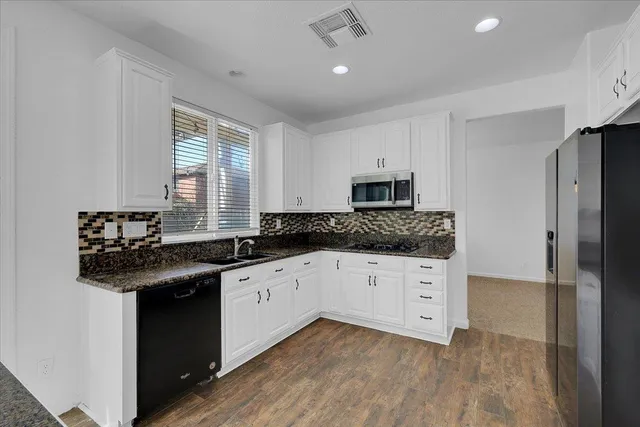 a kitchen with granite countertop a sink stainless steel appliances and white cabinets