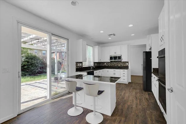 a kitchen with a refrigerator a stove top oven and a dining table with wooden floor