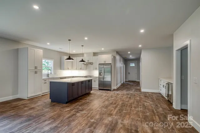 a room with stainless steel appliances kitchen island granite countertop a refrigerator and a sink