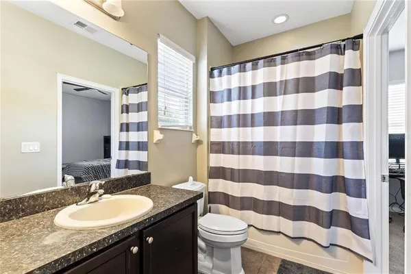 a bathroom with a granite countertop sink a toilet a mirror and shower curtain