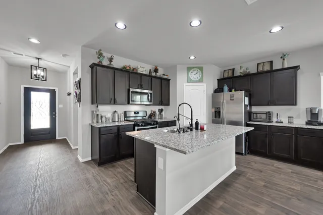 a large kitchen with stainless steel appliances granite countertop a stove top oven a sink dishwasher a refrigerator and a dining table with wooden floor