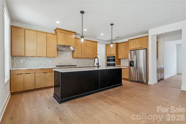 a kitchen with stainless steel appliances granite countertop a refrigerator a sink dishwasher a stove and white cabinets with wooden floor