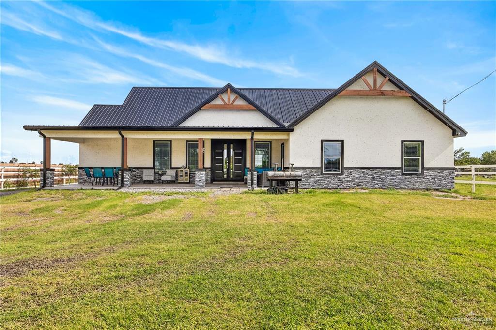 463 Eldora Road Donna, TX 78537 - Photo 1 of 1 Modern farmhouse-style exterior featuring a dark metal roof, light-colored stucco siding, and a stone veneer foundation