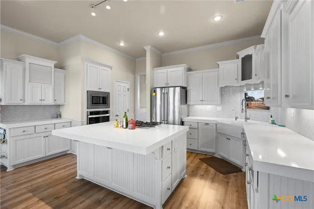 a kitchen that has a lot of white cabinets and stainless steel appliances