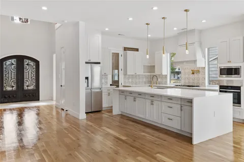 a large kitchen with stainless steel appliances kitchen island granite countertop a stove a sink a refrigerator and white cabinets with wooden floor