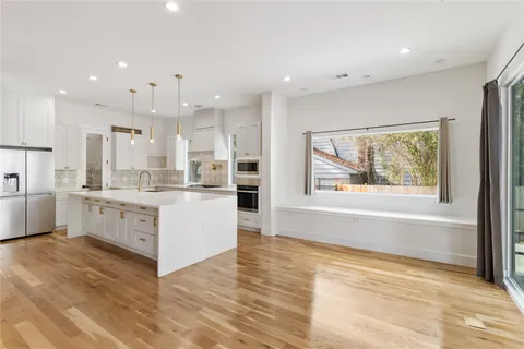 a kitchen with stainless steel appliances granite countertop a stove a sink and white cabinets with wooden floor next to windows