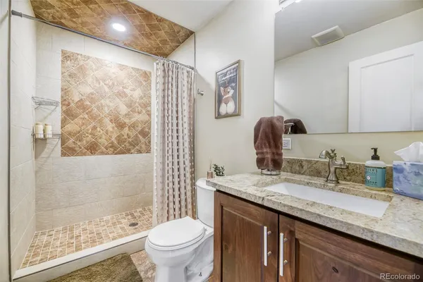 a bathroom with a granite countertop sink toilet and painting on the wall