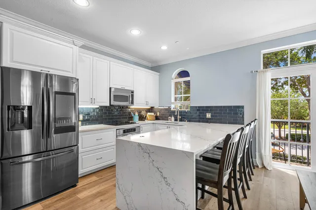 a kitchen with stainless steel appliances granite countertop a stove a refrigerator a sink a stove and white cabinets with wooden floor