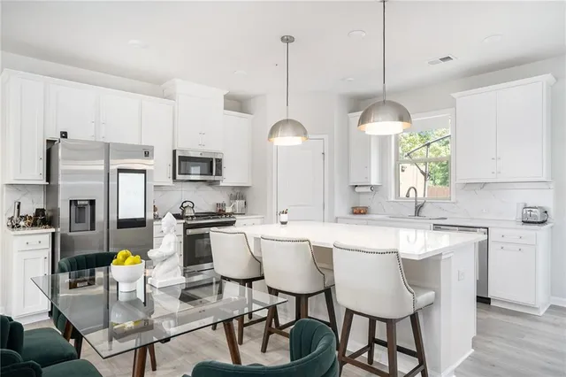 a kitchen with stainless steel appliances a dining table chairs stove and white cabinets