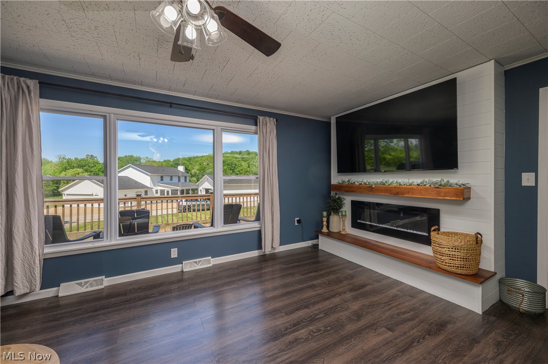 6105 Wolf Run Road Southeast Dennison, OH 44621 - Photo 16 of 35 Spacious room featuring wood-finish flooring, a contemporary electric fireplace with a wood mantle, and an expansive window wall overlooking a wood deck