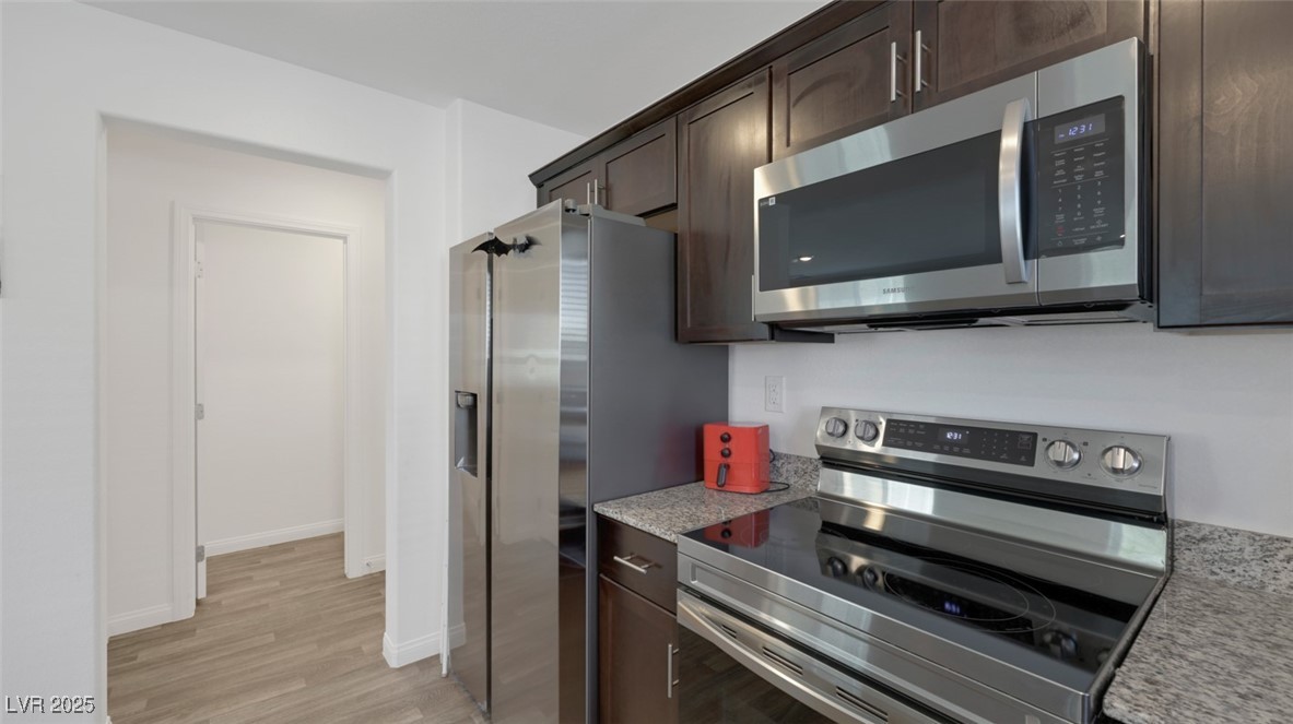 12346 Indigo Montage Road, Unit 4 Las Vegas, NV 89183 - Photo 10 of 27 Kitchen featuring dark brown cabinets, stainless steel appliances, light wood finished floors, and light stone countertops