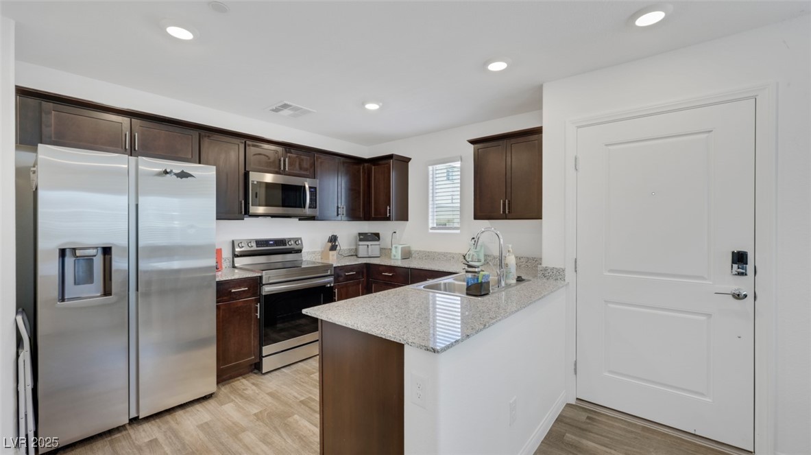 12346 Indigo Montage Road, Unit 4 Las Vegas, NV 89183 - Photo 8 of 27 Kitchen with stainless steel appliances, dark brown cabinets, light wood-style floors, a peninsula, and light stone countertops