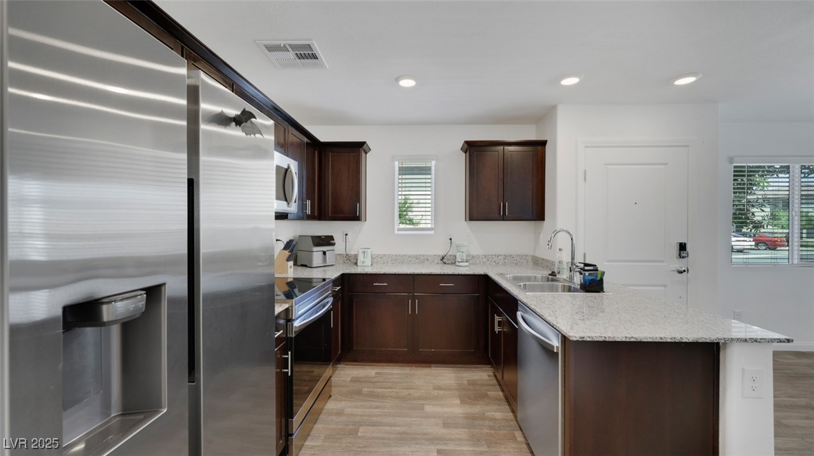 12346 Indigo Montage Road, Unit 4 Las Vegas, NV 89183 - Photo 9 of 27 Kitchen featuring appliances with stainless steel finishes, dark brown cabinets, a peninsula, light wood-type flooring, and light stone countertops