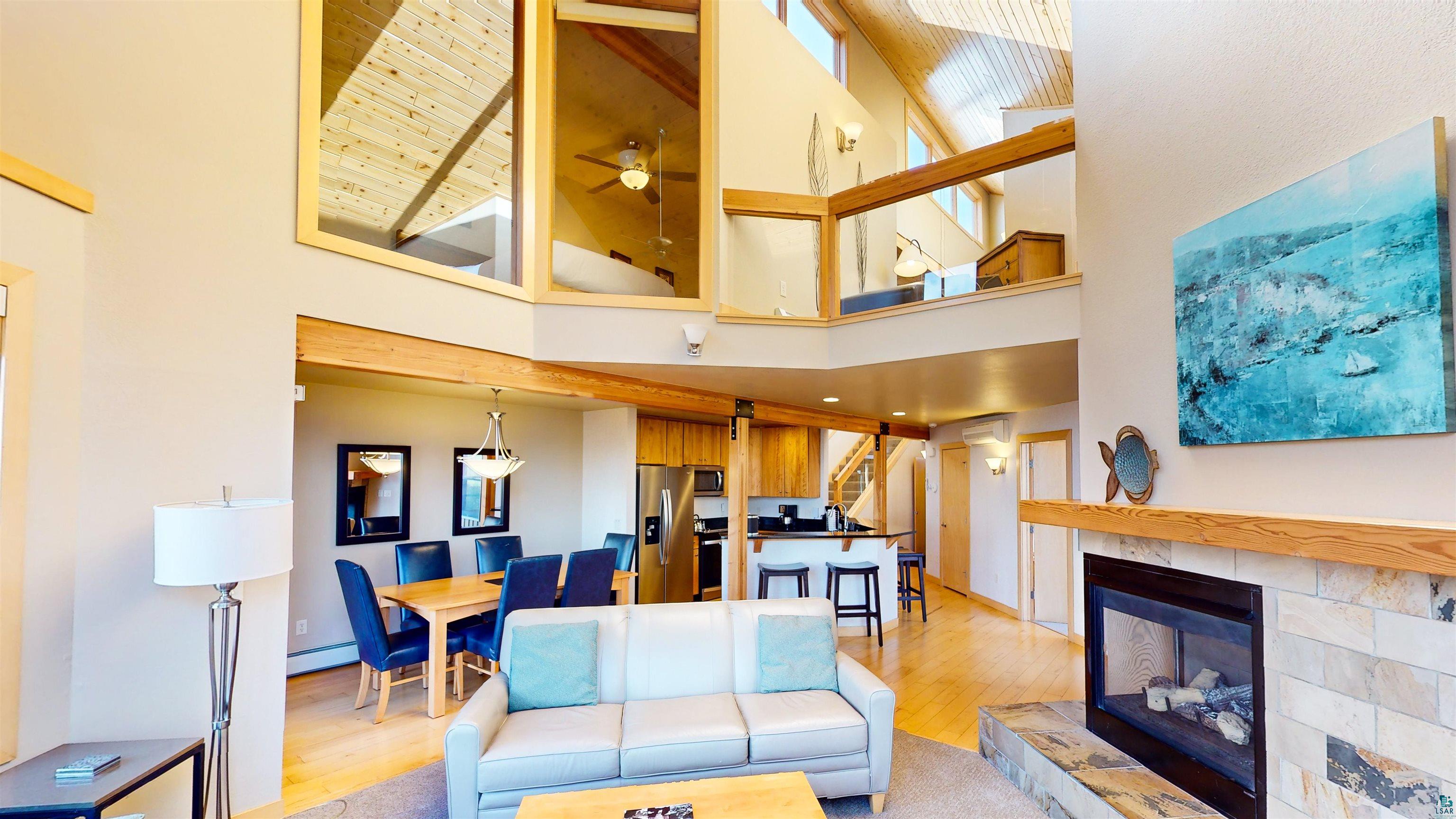 40 Surfside Drive, Unit 5D Tofte, MN 55615 - Photo 5 of 37 Expansive living area featuring a stacked stone fireplace with a substantial hearth, wood-finish flooring, and a two-story vaulted ceiling with exposed beams