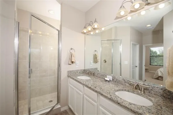 a bathroom with a granite countertop double vanity sink mirror and shower