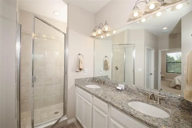 a bathroom with a granite countertop double vanity sink mirror and shower