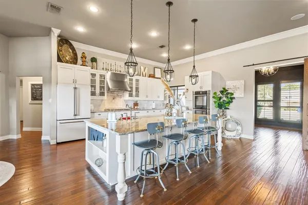 a kitchen with stainless steel appliances kitchen island granite countertop a refrigerator a stove a dining table and chairs with wooden floor